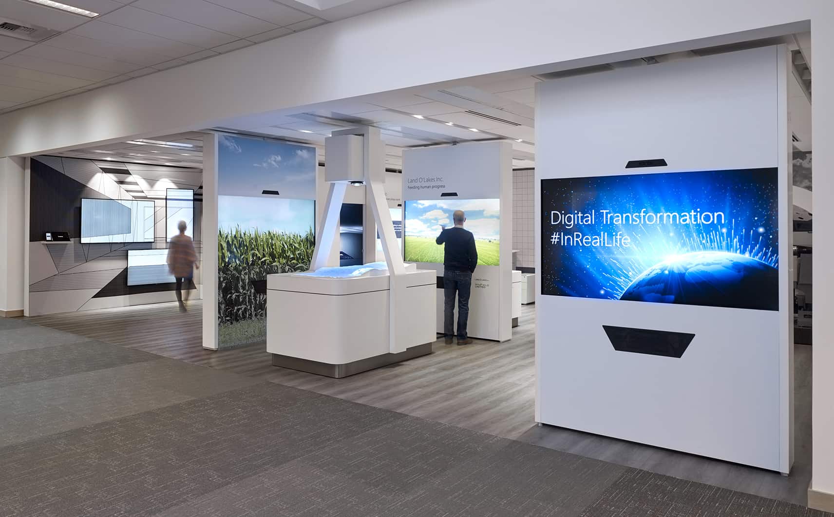 Sleek modern office with digital globes, #InRealLife text, nature images; two people interact; bright lighting enhances futurism.