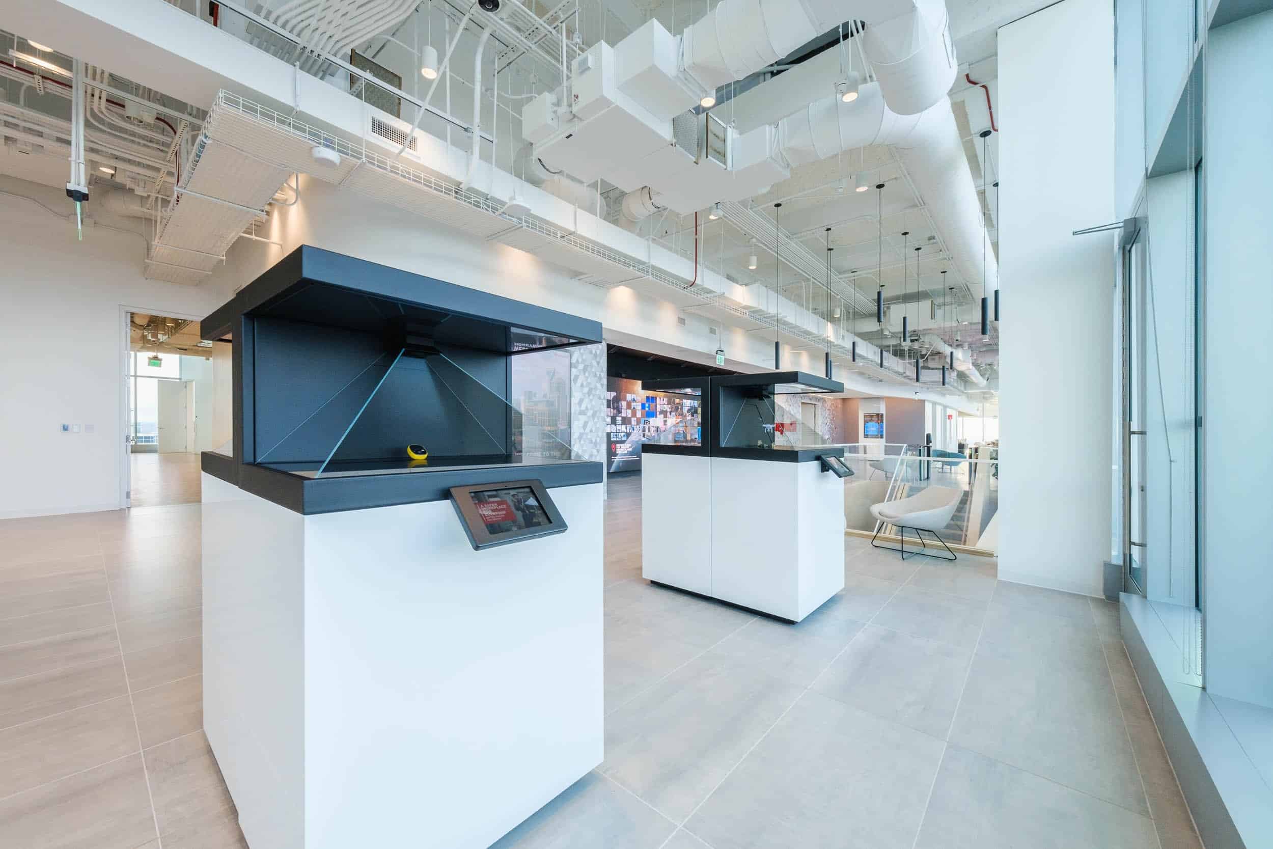 Modern minimalist office with two tablet kiosks, high ceilings, exposed ductwork, natural & artificial lighting, large windows.