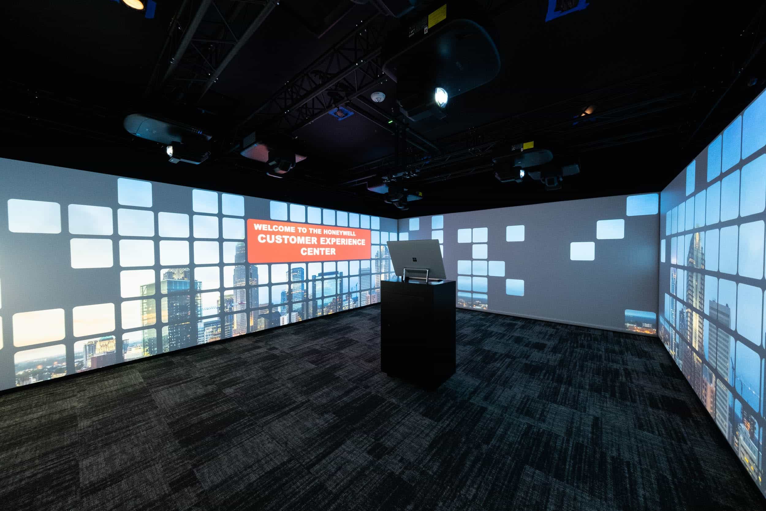 Futuristic room with video wall showing cityscape & patterns. Podium with laptop reads Welcome to the Future: Customer Experience Center.