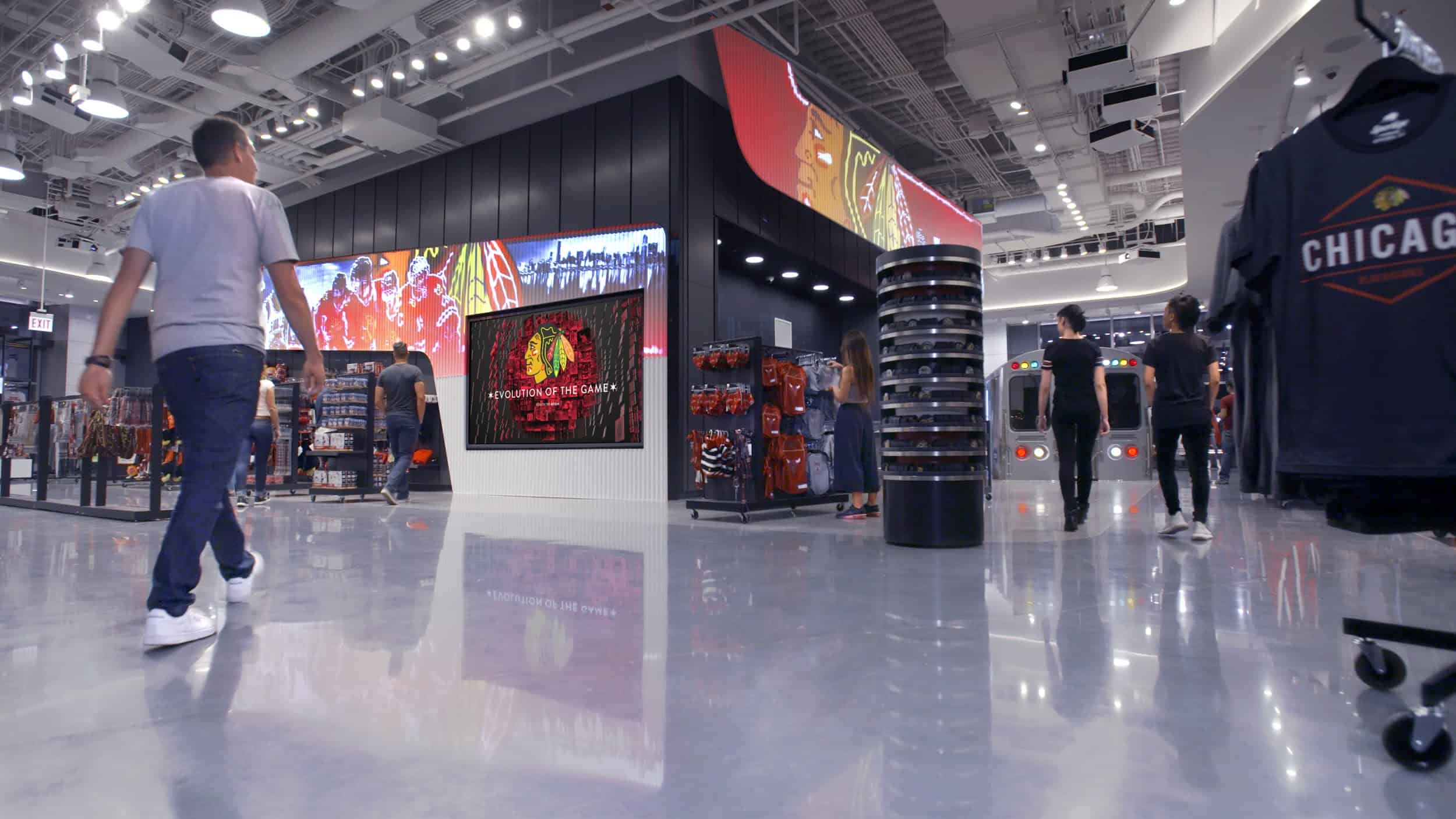 Modern store interior with shoppers, digital screen showing sports images, Chicago shirts on shelves, bright lighting.