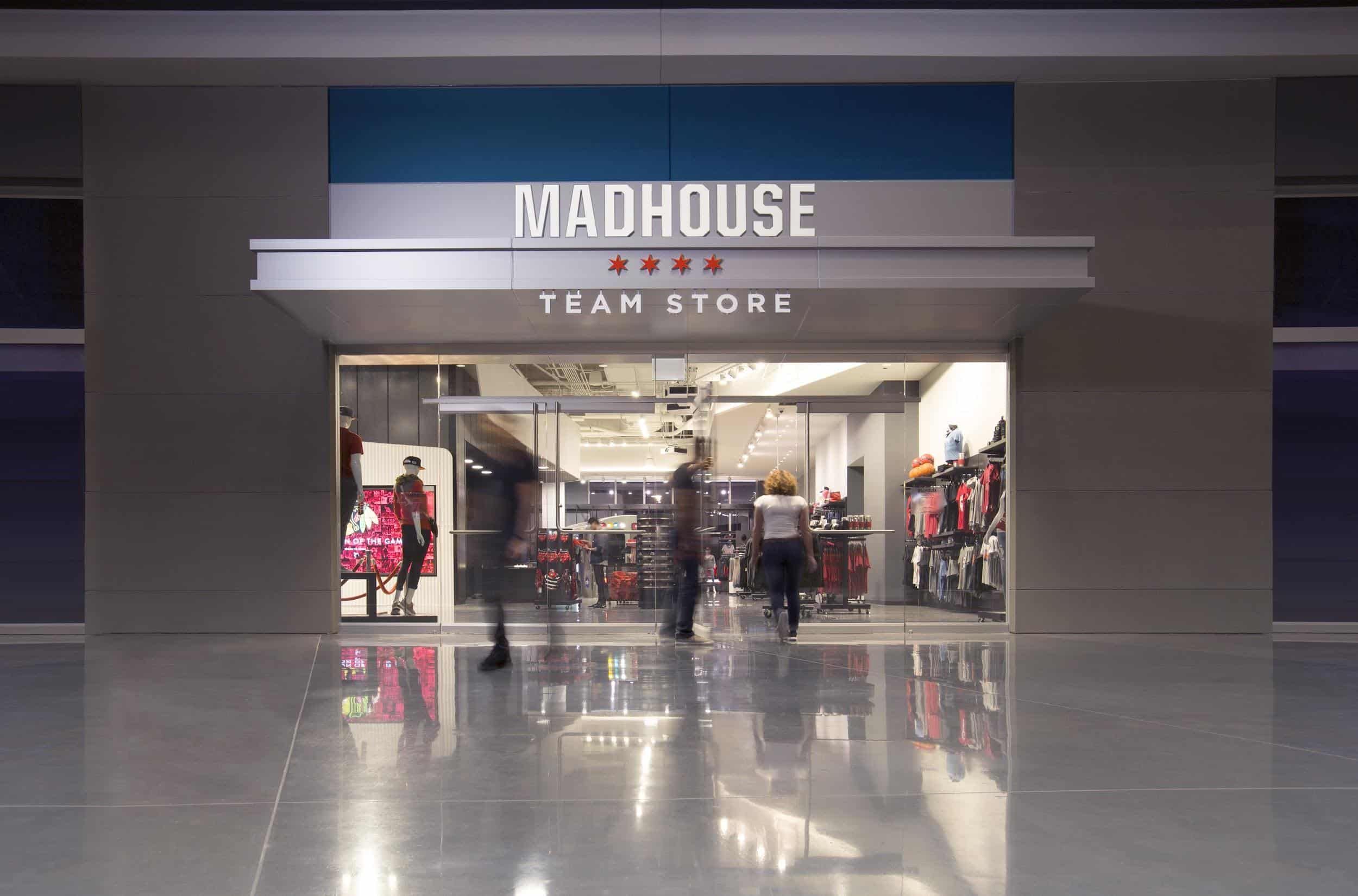 Madhouse Team Store: Modern glass entrance, sports gear on racks; bustling shoppers inside, glossy reflective floor.